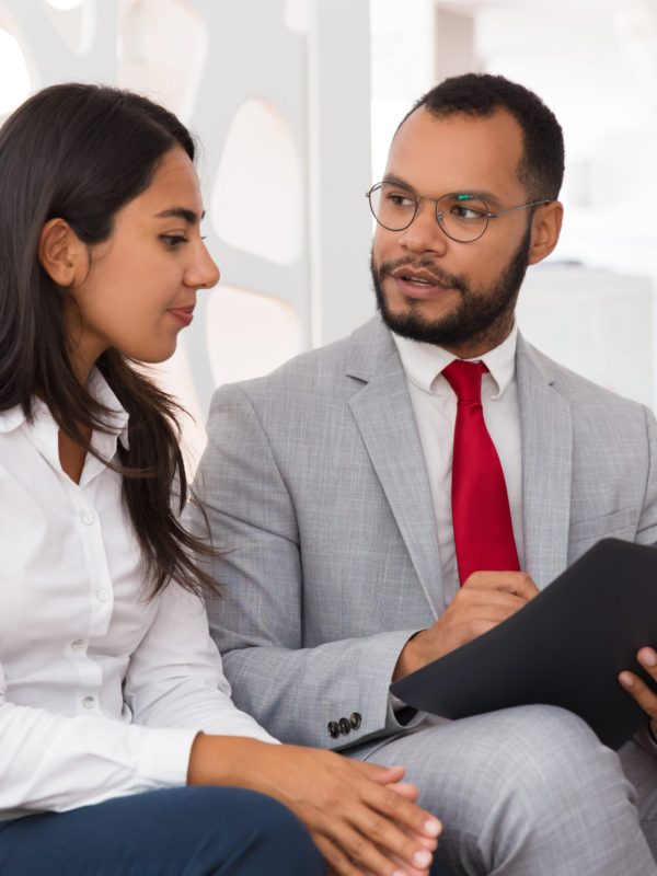Legal expert explaining document specifics to customer. Business man and woman sitting on office couch with open folder and discussing papers. Expertise concept